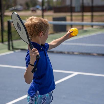 Image of young boy holding a pickleball paddle in one hand and a ball in the other as he gets ready to serve the ball.