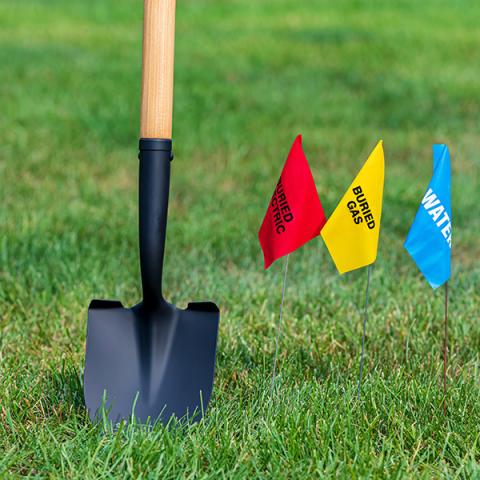 Shovel in grass next to water, gas line flags