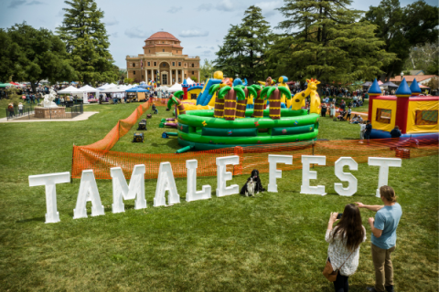 Image of Tamale Festival Event in Sunken Gardens with large block letters of the event name in the foreground and bounce houses and event activities underway in the background.