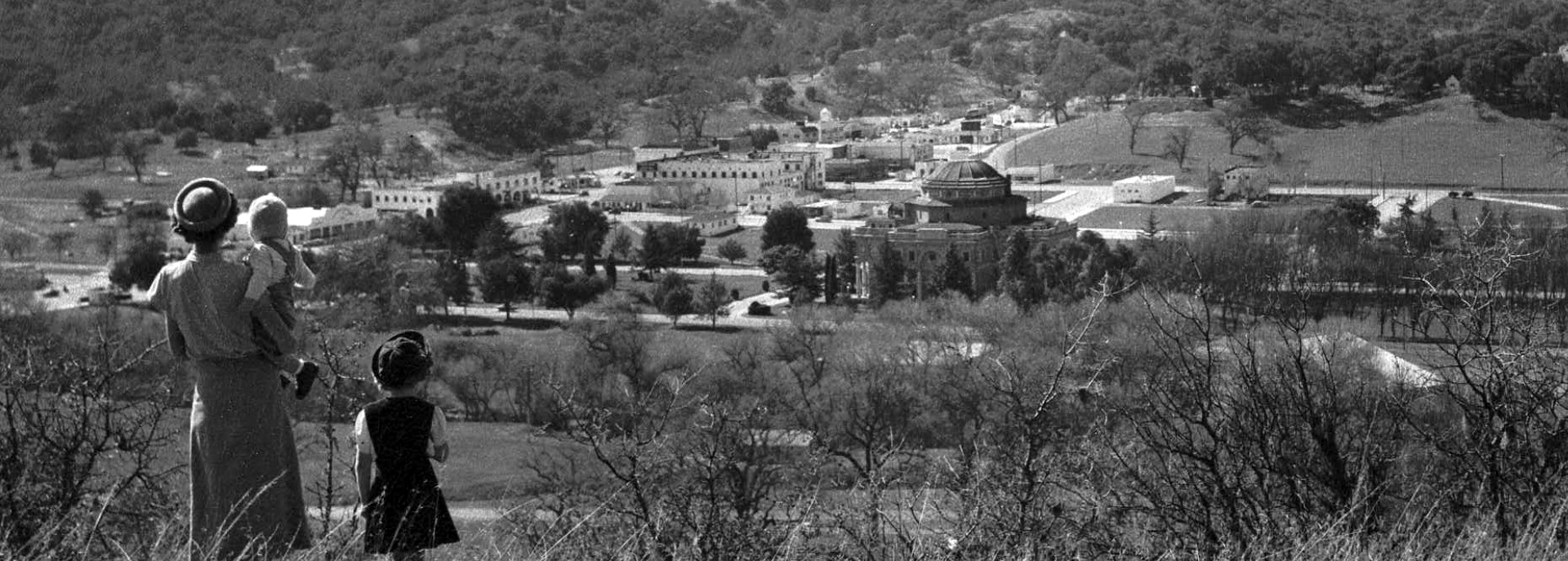 Historic photo of a woman with two children looking down at old downtown Atascadero from atop a hill.