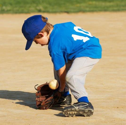 Young boy leaning down to catch a baseball.