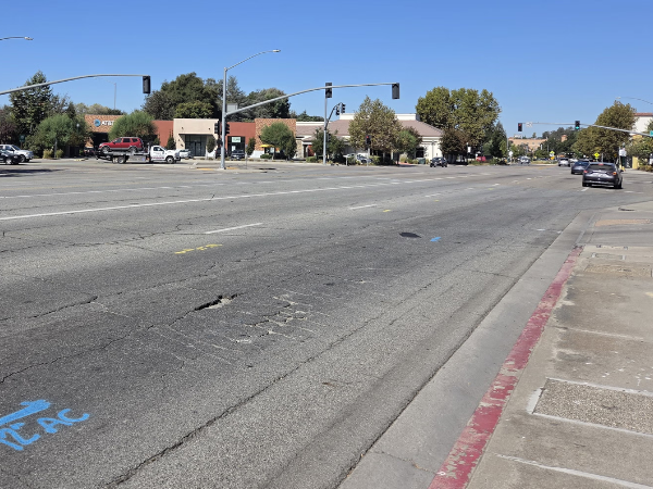 Landscape photograph of a multi-lane street intersecting with another multi-lane street. The pavement is visibly cracked and in need of repair.