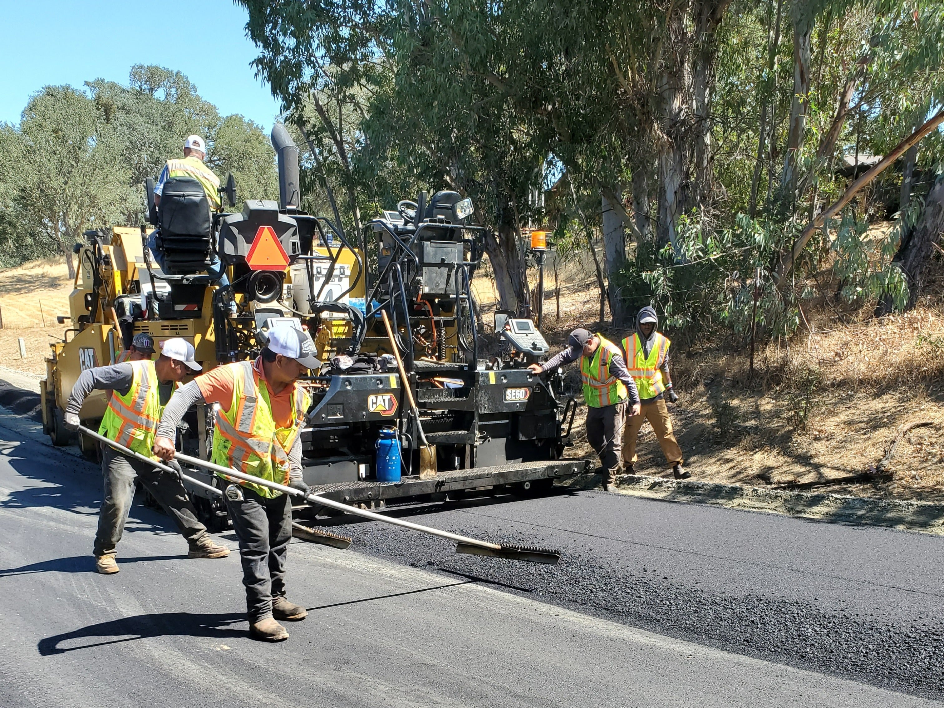 Paving crew in hi-vis vests working on freshly paved road. 