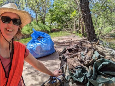 Volunteer at a creek cleanup event with collected trash and debris.