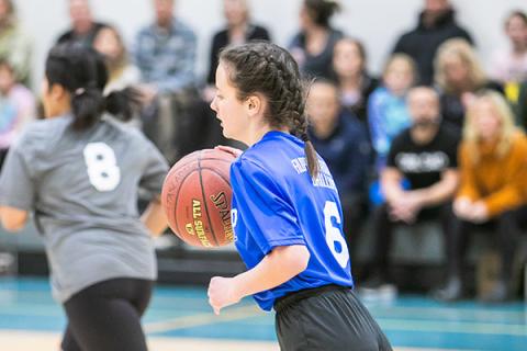 Basketball game in action with girl in profile dribbling the ball and running.