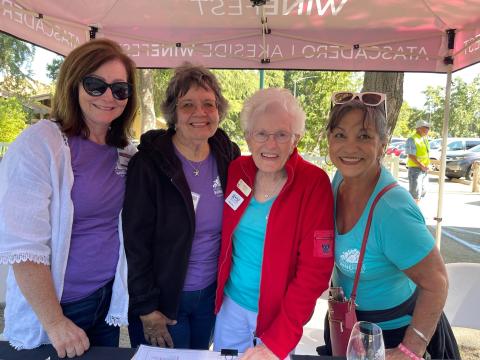 Image of four volunteers at the Wine Festival leaning in for a group photo.