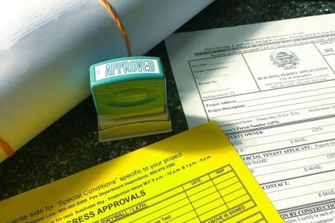 Close-up of a building department permit counter with a permit card, application, a set of plans, and an approval stamp