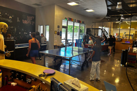 A wide shot of the Teen Center full of teens playing games such as air hockey, ping pong, pool, and mini basketball.