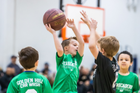 Youth basketball game featuring a boy jumping to pass the ball while another boy attempts to block the play.