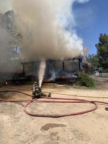 Firefighter seated on the ground while spraying water from a hose onto an active structure fire.