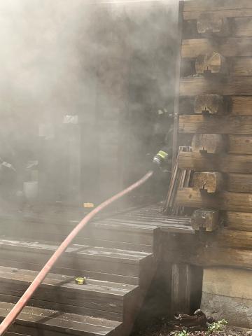 Smoke-filled scene showing part of a firefighter standing in the doorway of a structure fire while holding a hose.