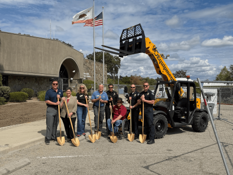 City Manager, City Council Members, the Police and Fire Chiefs, and a Police Commander hold ceremonial gold shovels in front of the Atascadero Police Station at the Police Station groundbreaking ceremony, with construction fencing and heavy equipment visible in the background.