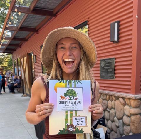 Picture of Emma Rhoads with TJA Advertising, holding The Central Coast Zoo's new Activity Book, which she designed.