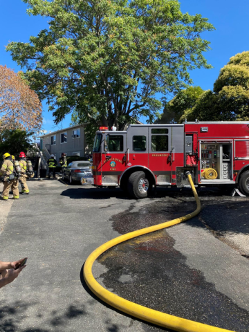 Red fire engine at the scene of the Atascadero Robles Fire, with a long yellow hose on the pavement and firefighters in protective gear nearby.