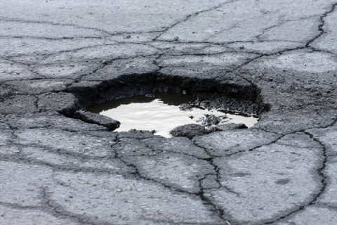 Pothole in the road with cracked asphalt all around.